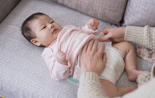 cropped shot mother’s hands fastening the fresh diaper for her lovely baby daughter who is