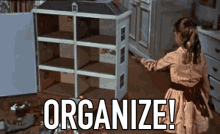 Girl arranging a dollhouse beside the word ORGANIZE! in a cluttered room. Funny magic, professional organizer.