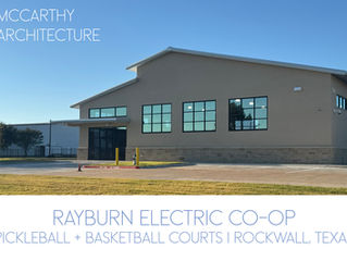 Exterior view of the nearly completed Rayburn Electric Co Op Recreational Facility in Rockwall, Texas, showing the modern facade with large windows, stone base, and finished parking area under a bright blue sky.
