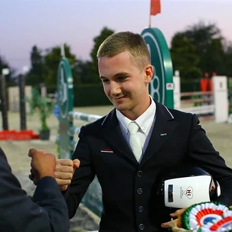 LoveHorses est heureux de présenter Matteo Rogiani, l'un de nos jeunes cavaliers les plus prometteurs, en train de serrer la main du directeur du concours qu'il vient de remporter. Le bonheur de Matteo est palpable, avec un large sourire sur le visage et les yeux brillants de satisfaction.