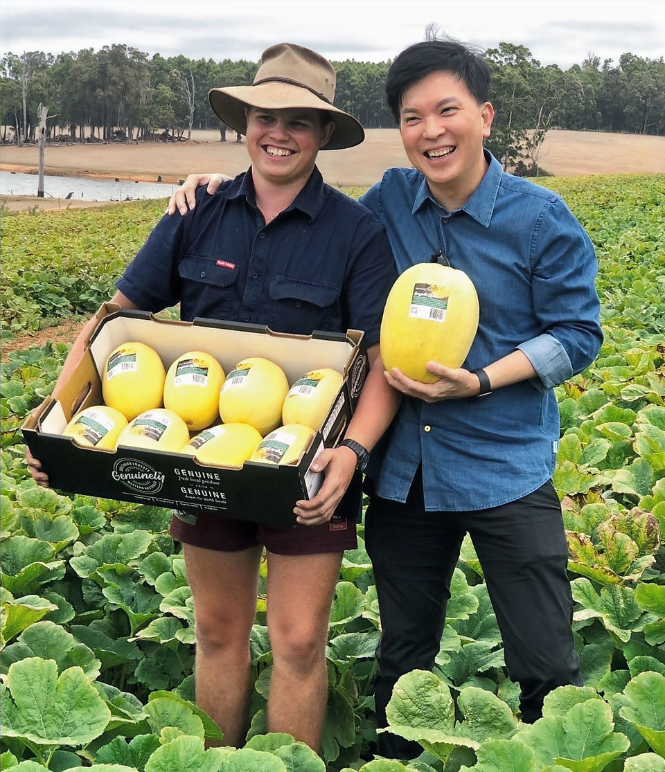 Two people in a field of green holding vegetables smiling at the camera