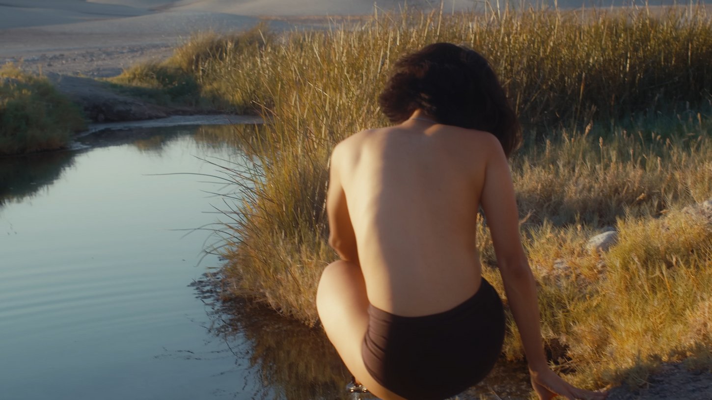 In the Stillness in Tecopa episode on Sauna Channel, a topless woman is shown crouching next to the Tecopa desert hot springs in California and connecting with nature.