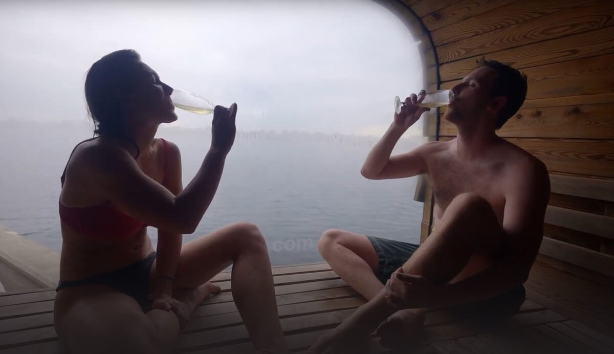 On the CopenHot episode of Sauna Channel, a couple drinks champagne while enjoying the sauna on the water at CopenHot in Copenhagen, Denmark