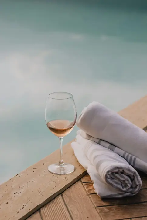 Wine glass next to pool with rolled white towels
