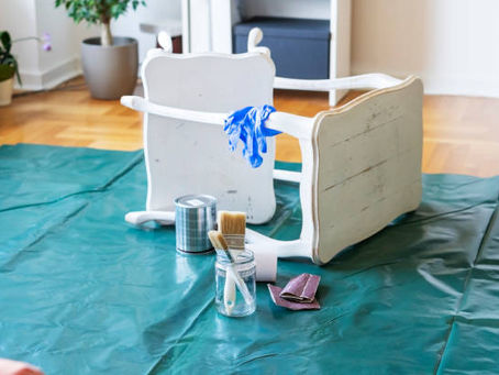 White chair flipped over on a drop cloth with paint can, brushes, and sanding tools nearby