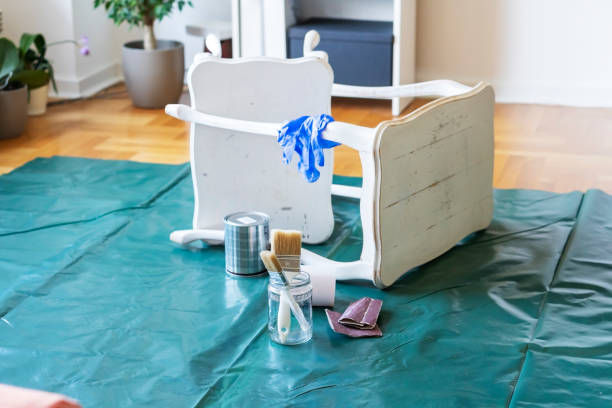 White chair flipped over on a drop cloth with paint can, brushes, and sanding tools nearby