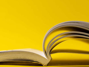 Open book with pages arcing upward on a bright yellow background, creating a clean, minimal still life.