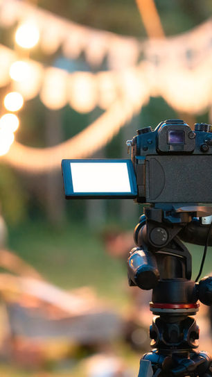 Camera on a tripod focusing on blurred people and string lights in a festive outdoor setting. Warm and inviting atmosphere.