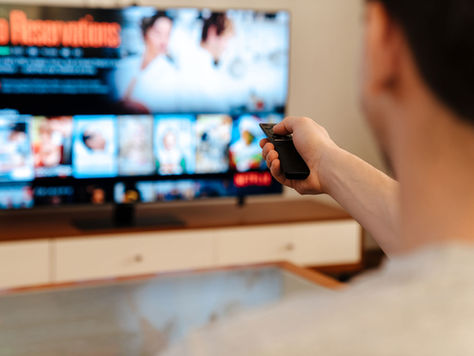 Person points a remote at a TV streaming menu showing No Reservations in a cozy living room.
