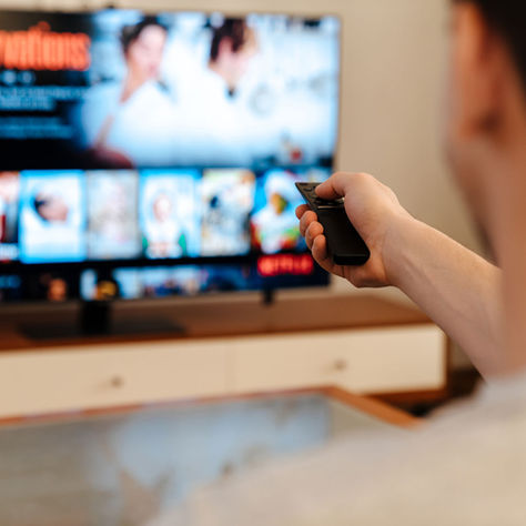 Person points a remote at a TV streaming menu showing No Reservations in a cozy living room.