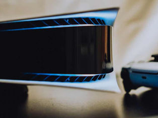 Close-up of a PlayStation 5 console and controller on a tabletop, with blue light accents and a sleek, futuristic look.