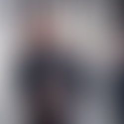 Smiling woman in winter coat and scarf stands in snowy forest. Two people in the background, snow falling, creating a serene atmosphere.