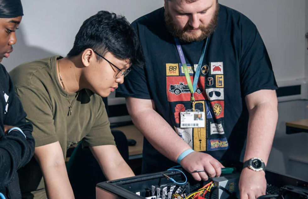 Three people lean over a computer tower and wiring in a classroom lab, focused on a tech project.