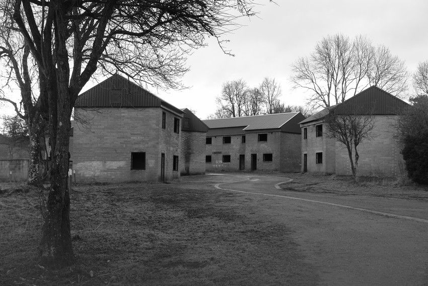 Black-and-white view of abandoned brick buildings around a curved driveway, with leafless trees and an eerie, empty mood.