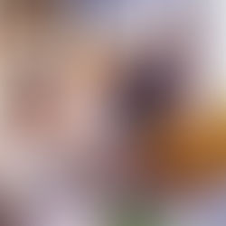 Smiling group in an office, celebrating. A woman offers cake with lit candles to a seated woman in yellow. Bright, cheerful setting.