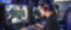 Gamer with headphones focused on a video game. Colorful keyboard, intense screen reflections, dim gaming room setting.