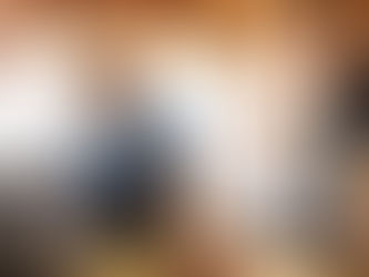 Man in glasses and apron working on laptop in bike shop. Bright, industrial setting with exposed beams and hanging bikes in background.