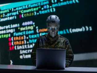 Robot in camo outfit using a laptop, with colorful programming code on a dark screen in the background. Mysterious, tech-focused setting.