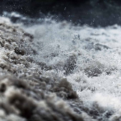Raging brown river water splashes violently, creating frothy waves. A dark, blurred background adds to the chaotic, intense scene.