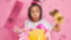 Young girl with pigtails holds a dirty sponge and pink mop, standing against a handprint-covered pink wall, looking frustrated.