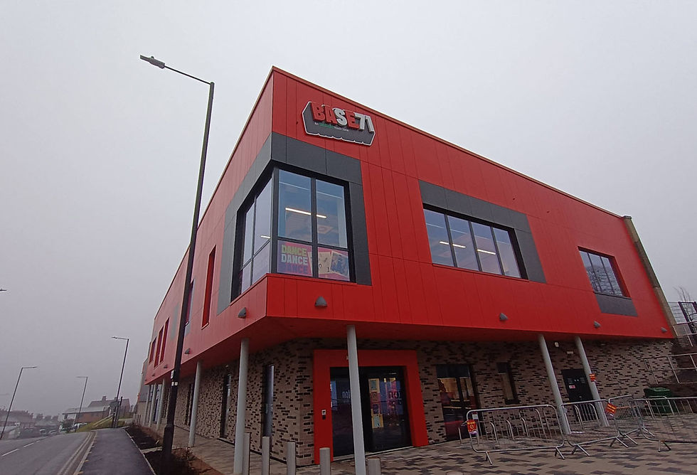 Red building labeled BASE 71, with large windows. Poster reads "DANCE DANCE DANCE" inside. Overcast sky, street and lamp posts in view.