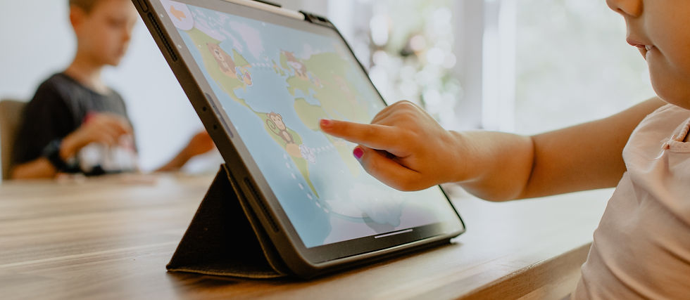 Child points at a tablet displaying a colorful animal world map, with another child blurred in the background.