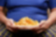 Faceless man in blue shirt eating some Chips, this can impact weight and walking Gait.
