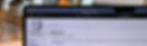 Laptop screen showing the Wikipedia homepage in a web browser. Background is softly blurred with warm tones, suggesting a cozy indoor setting.