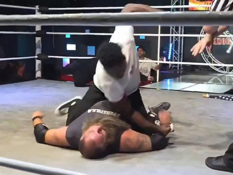 Raja Jackson pins opponent in the ring. Referee watches. Crowd in the background. Action is intense and dynamic, with vibrant lighting.