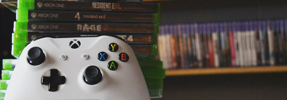 White Xbox One controller in front of stacked game cases, including Resident Evil and Rage 2, with blurred shelf background