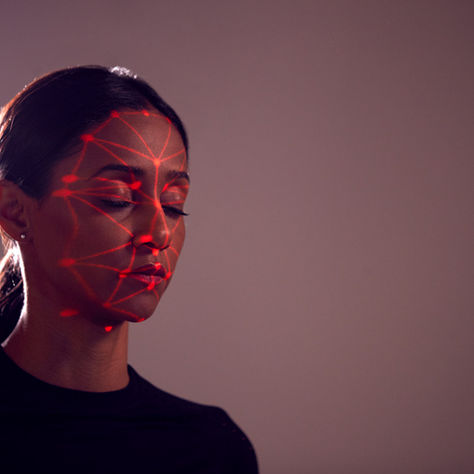 Woman with closed eyes in dark setting, red geometric light pattern projected on her face, conveying a calm, futuristic mood.