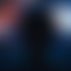 Silhouetted person wearing headphones watches a wall of glowing screens in a dark blue room, creating a focused mood