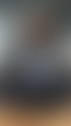 Woman meditates on office table, eyes closed, amid colleagues gesturing animatedly. Modern office setting, focused, calm mood.