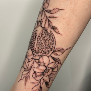 fineline illustrative linework tattoo of pomegranate fruit on a branch, flowers and leaves in black and grey, fineline tattoo artist in newcastle upon tyne, england, uk