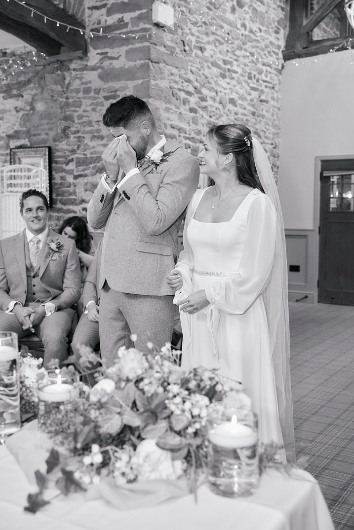 Groom wiping tears of joy at wedding reception as bride smiles