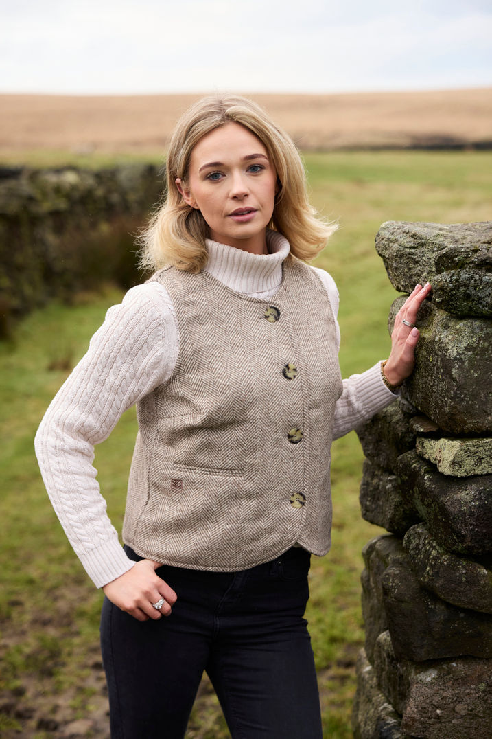 Woman in beige vest and sweater by stone wall