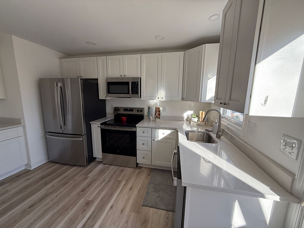 Bright modern kitchen with white cabinets, stainless steel fridge and oven, sunlit counters, sink by window, and wood-look floor