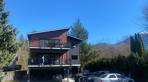 A three-storey co-living home with vehicles in the foreground, trees and a hillside in the background.