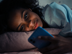 Woman lying in bed staring at her phone's screen.