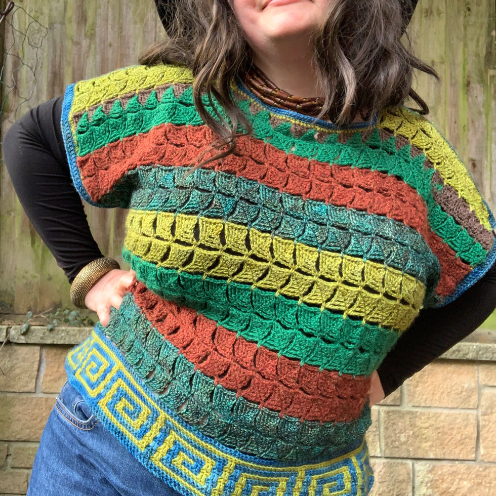 Woman wearing colourful crochet shirt, smiling, posing in front of a brick wall.