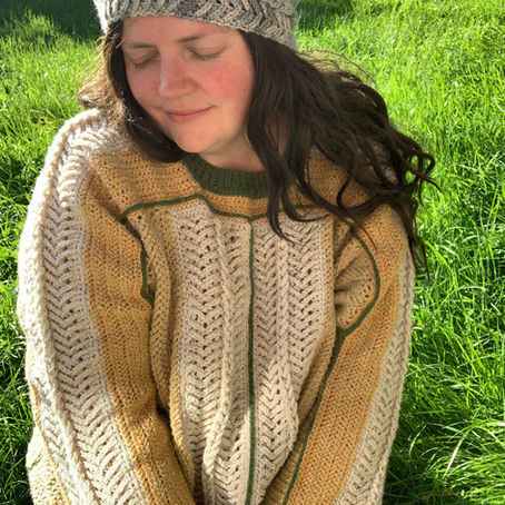 A woman wearing a textured crochet sweater in cream and beige on a grass background.