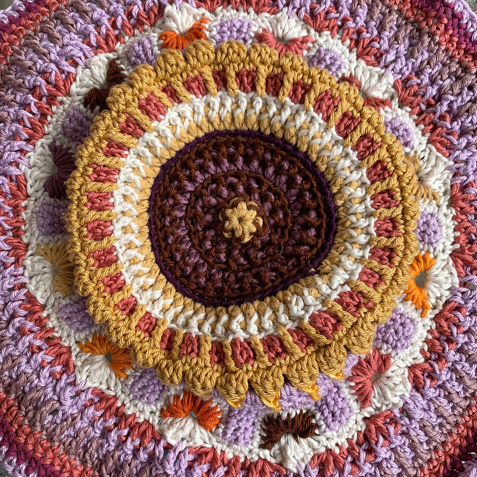 Colourful crochet mandala with concentric circles in pink, orange, brown, and purple hues. Textured pattern creating a warm, vibrant mood.