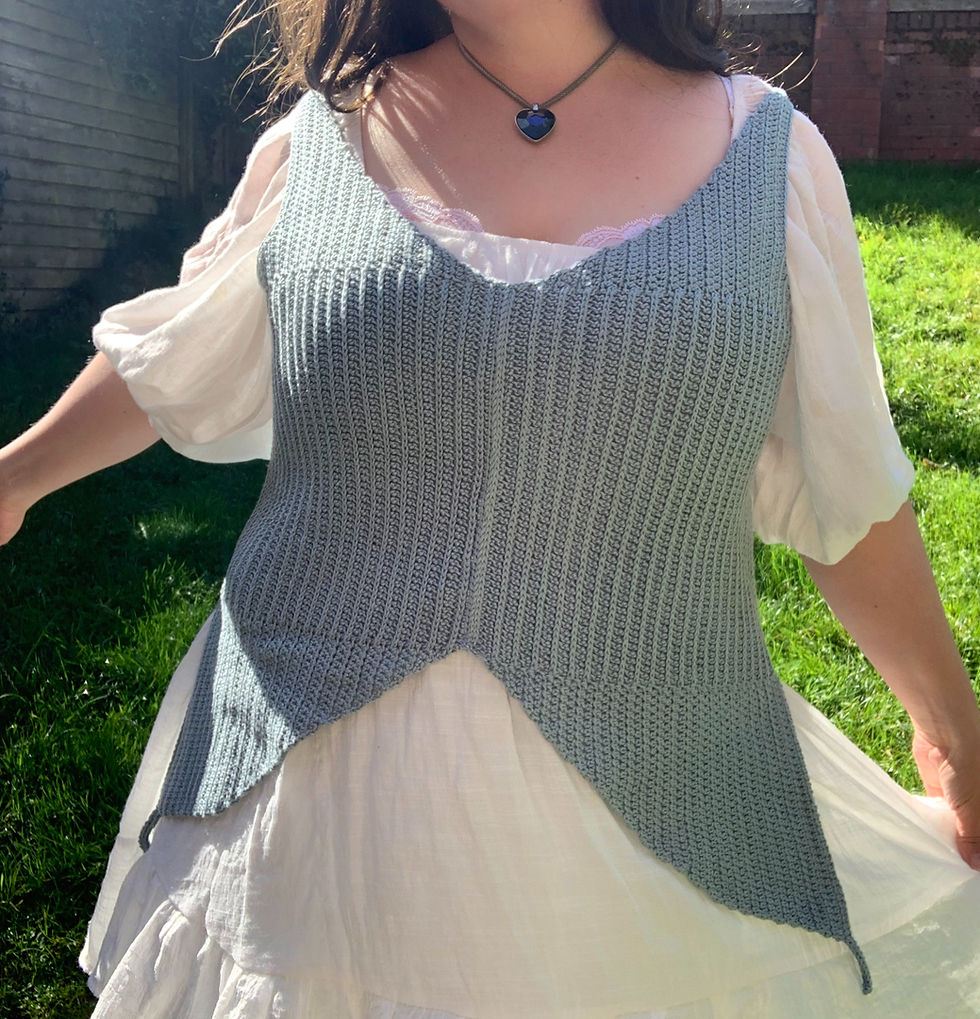 Woman in a white dress and pale blue crocheted vest twirling in a sunlit garden, wearing a heart-shaped necklace. Grass and wooden fence in background.