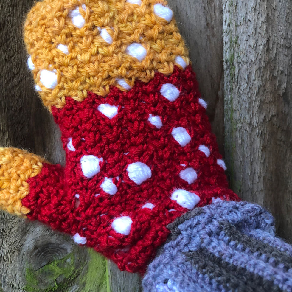 Crocheted red and yellow mitten with white spots and grey cuff on hand.