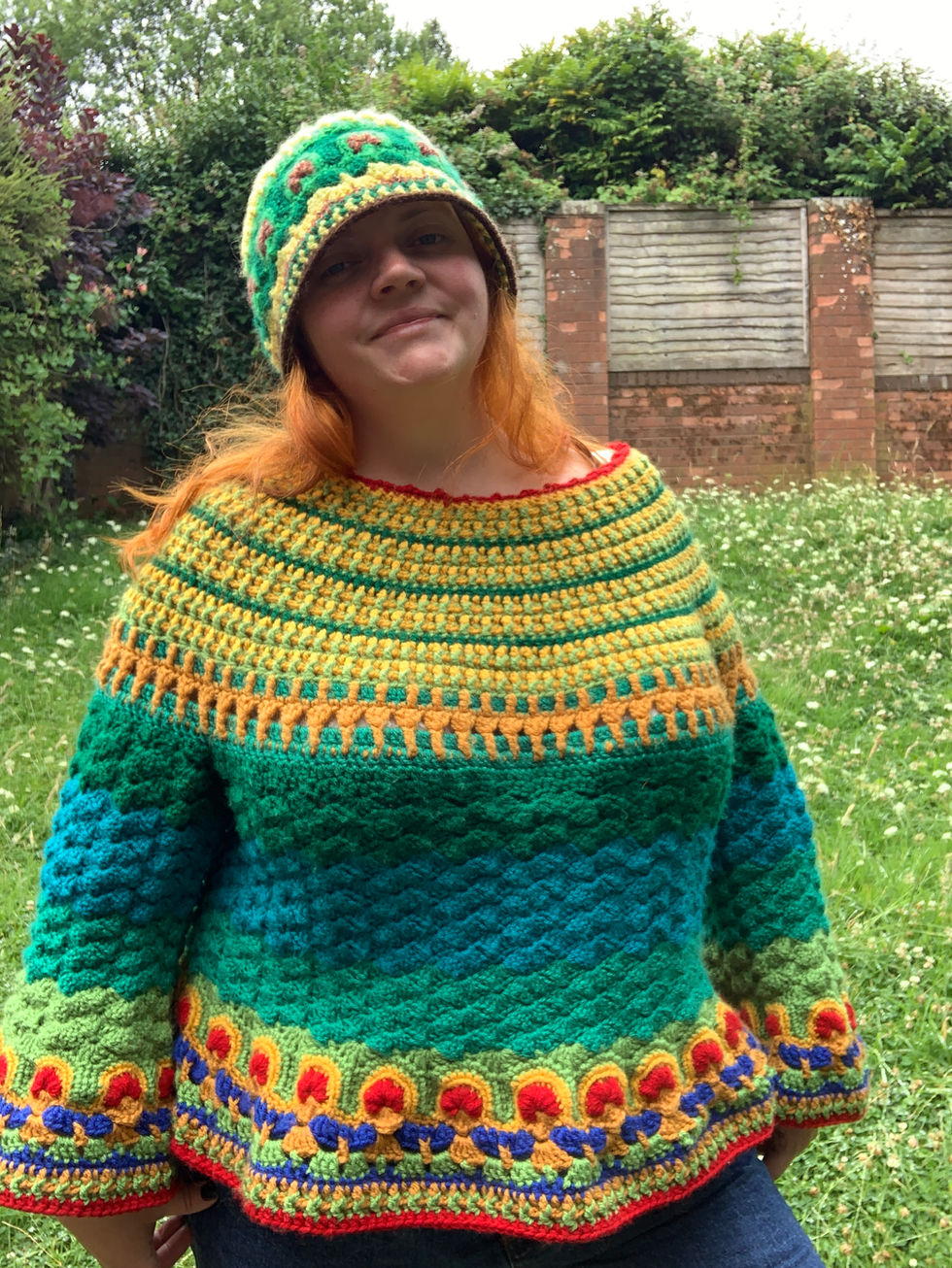 Woman wearing handmade crochet hat and sweater smiles outdoors in garden.