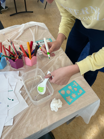 A young person using a ceramic spoon and colourful pens to create floating artwork, with a bowl of water ready for the design to be released from the spoon.