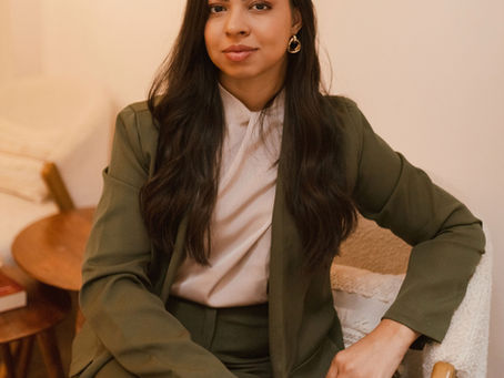 Psicóloga vestindo um traje social verde e bege com uma pose acolhedora