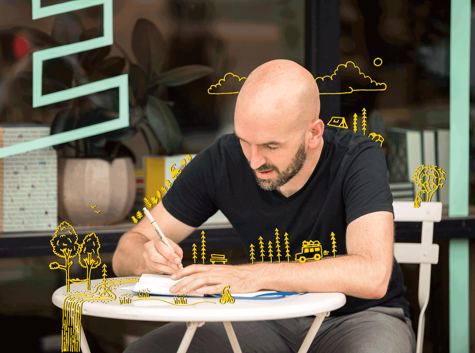 Artist drawing at table with trees and clouds drawn on and around him