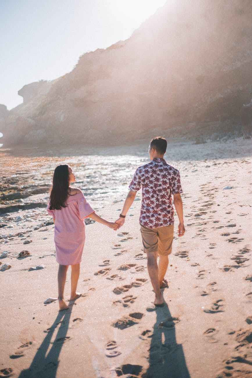 couple holding hands walking on seashore