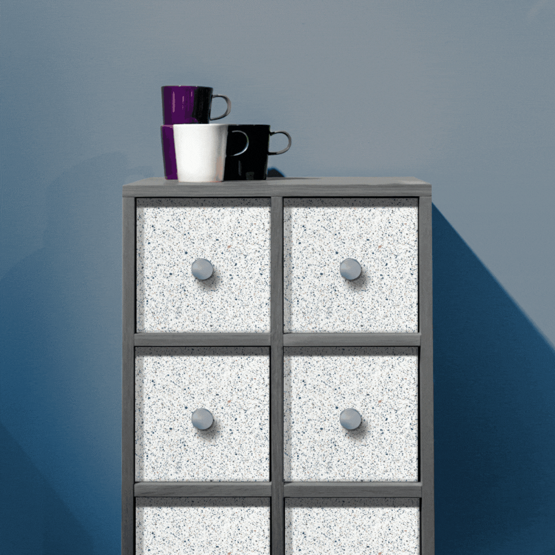 Gray cabinet with six Corian Quartz speckled drawers, topped by three stacked mugs—purple, white, and black. Blue gradient wall sets a calm mood.